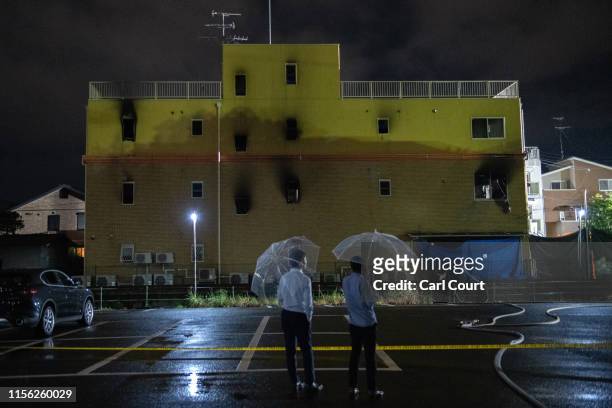People hold umbrellas as they pause next to the Kyoto Animation Co studio building after it was set ablaze by an arsonist on July 18, 2019 in Kyoto,...