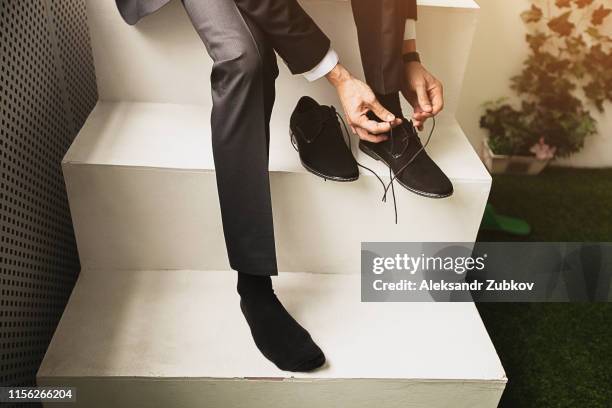 the man, a businessman, an entrepreneur or the groom sits on a white ladder and a new tying shoelace black suede shoes business, close-up. the concept of business, entrepreneurship, fashion. - zapatos de ante fotografías e imágenes de stock