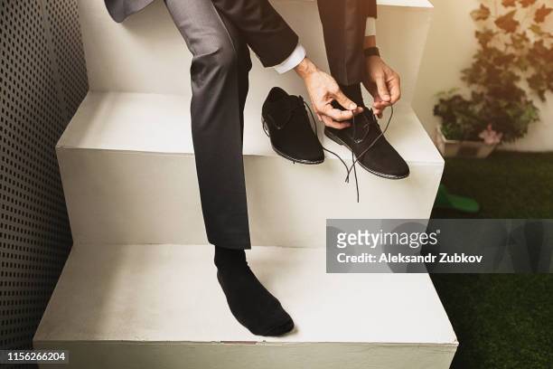 the man, a businessman, an entrepreneur or the groom sits on a white ladder and a new tying shoelace black suede shoes business, close-up. the concept of business, entrepreneurship, fashion. - suede shoe stock pictures, royalty-free photos & images