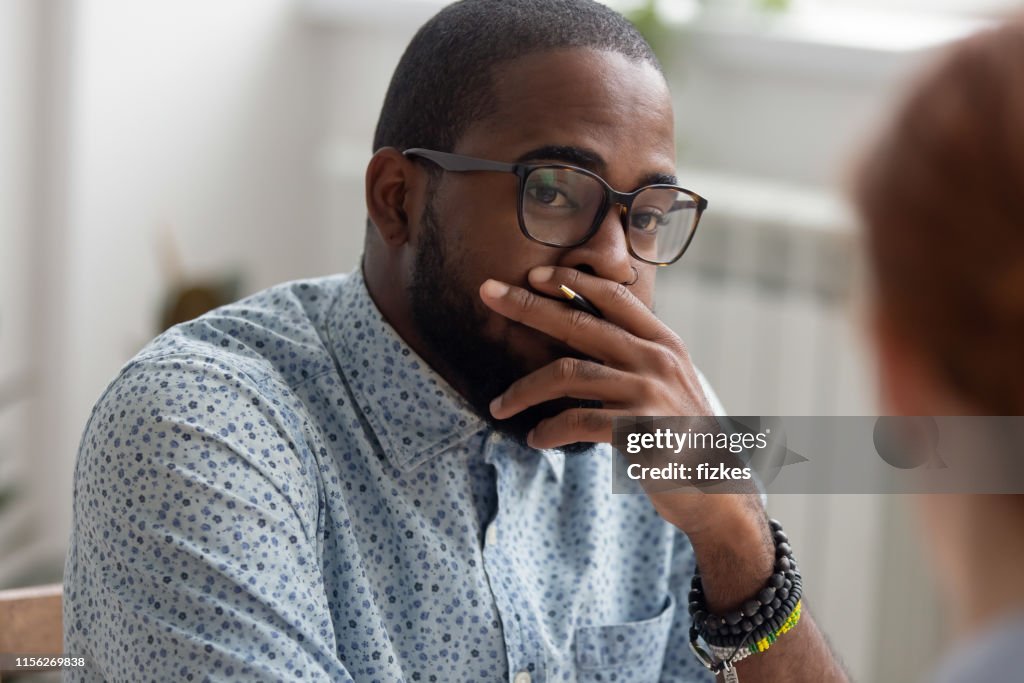 Unpleasantly surprised african-american businessman listening female caucasian coworker