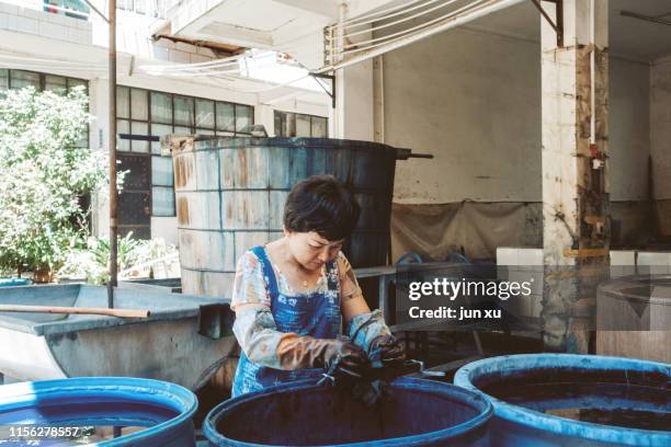 a worker who renders cloth in a blue dye vat - mani fili foto e immagini stock