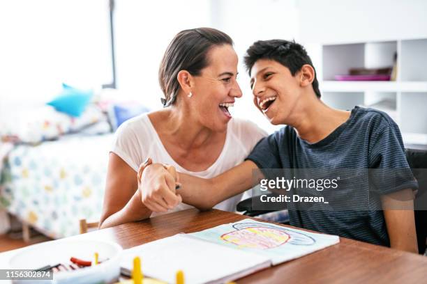 disabled latino teenager with celebral palsy and mother laughing. - wheelchair stock pictures, royalty-free photos & images