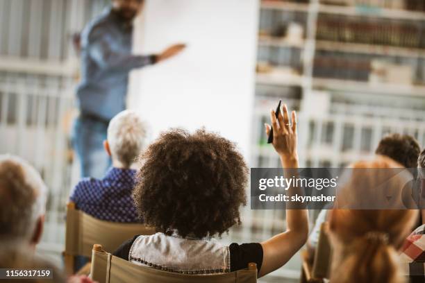 rear view of a woman raising her hand on a seminar. - questions answered stock pictures, royalty-free photos & images