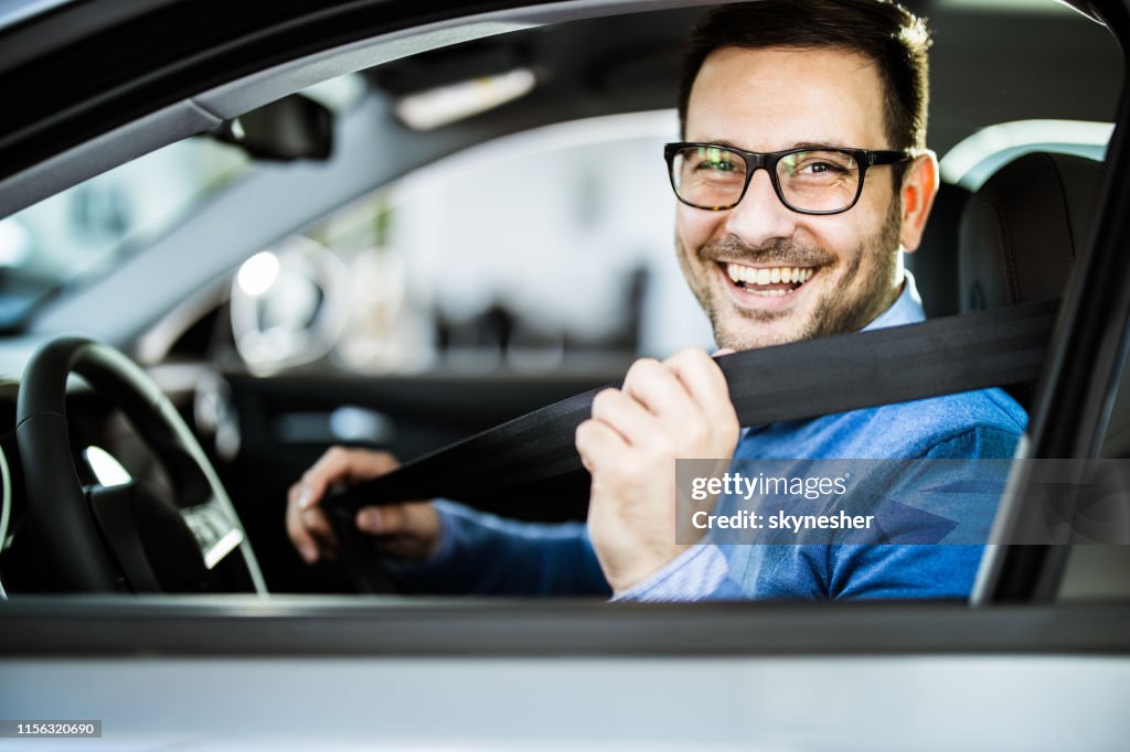 Buon uomo d'affari che fissa la cintura di sicurezza prima del suo viaggio in auto.