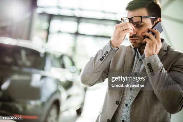 uomo d'affari che ha mal di testa mentre parla al cellulare in uno showroom di auto. - shopping male foto e immagini stock