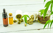 CBD cannabidiol oil glass bottles, pills flower buds and Cannabis leafs on bright wooden backdrop