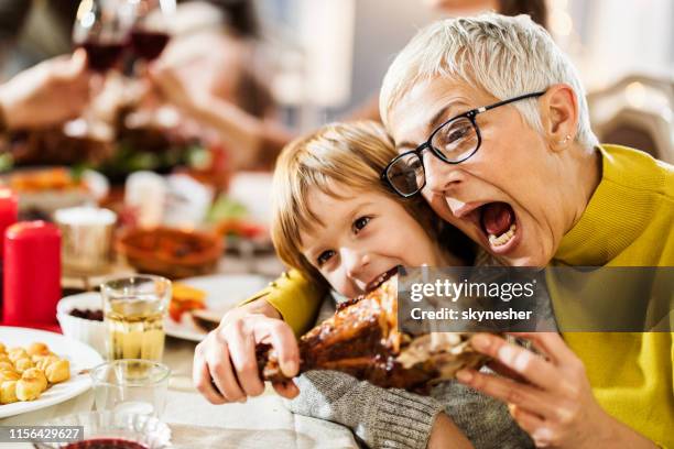 glückliche großmutter und ihr enkel haben spaß beim beißen truthahn bein zu hause. - turkey leg stock-fotos und bilder