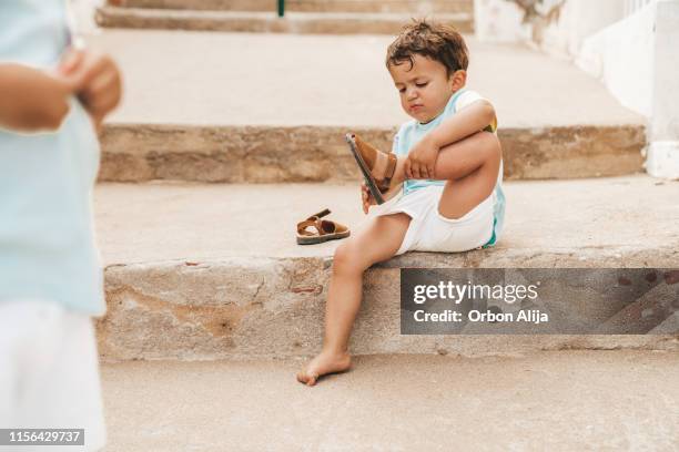 menino que põr sobre sapatas após um dia na praia - sandalia - fotografias e filmes do acervo