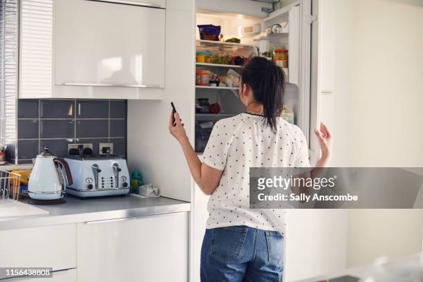 woman using smartphone - refrigerator stock-fotos und bilder