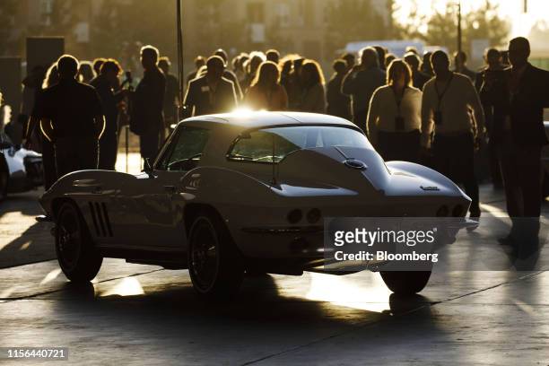 Attendees walk past a vintage General Motors Co. Chevrolet Corvette Stingray sports car on display ahead of an unveil event in Tustin, California,...