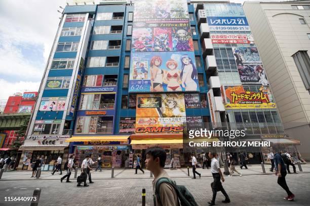 People walk past images of game and manga characters in the Akihabara district in Tokyo on July 19, 2019. - The devastating apparent arson attack on...