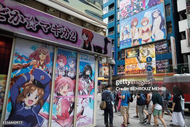 People walk past images of anime and manga characters in the Akihabara district in Tokyo on July 19, 2019. - The devastating apparent arson attack on...