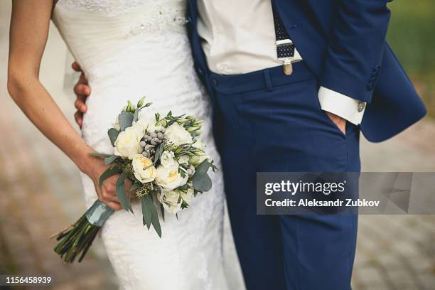 the bride in an elegant wedding dress is holding a beautiful bouquet of white roses, buds, green leaves and decorative items. embrace the newlyweds, the hands of the bride and groom close-up, outdoors - green dress stock pictures, royalty-free photos & images