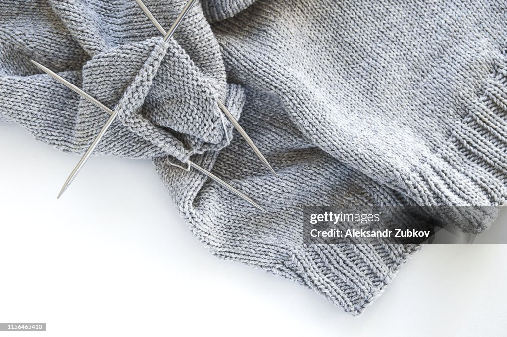 Incomplete knitting project with metal knitting needles close-up on a white background. Knitting a gray wool sweater. The concept of Hobbies, Creativity, crafts, handmade.