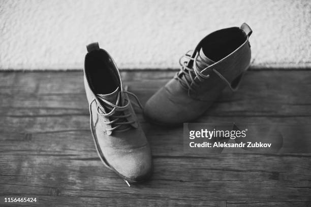 designer modern, worn, used, suede, women's shoes with a low heel, with untied laces, against a wooden floor and carpet. black and white photo, close-up. - suede shoe stock pictures, royalty-free photos & images