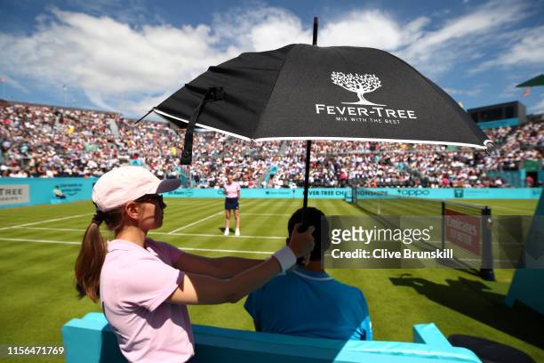 Ball girl holds an umbrella over the head of Christian Garin of Chile during a break in play during the First Round Singles Match between Christian...