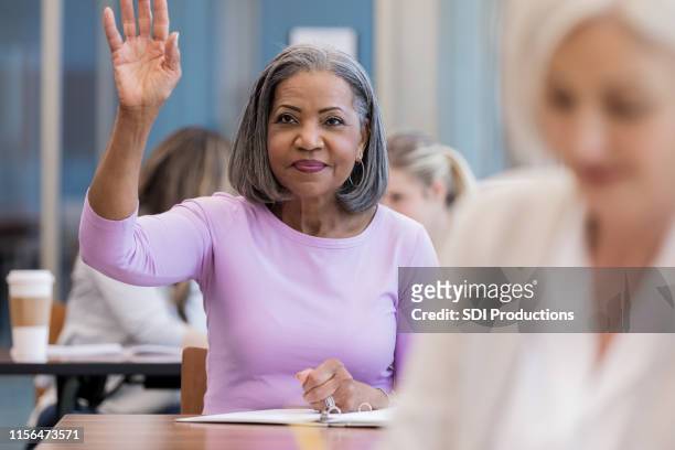 attractive mature african american woman raises hand in class - intelligence community stock pictures, royalty-free photos & images