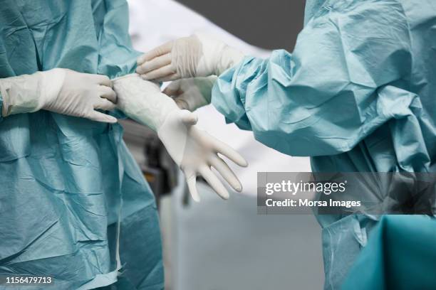 female doctor helping surgeon wearing glove - arbeitskleidung stock-fotos und bilder