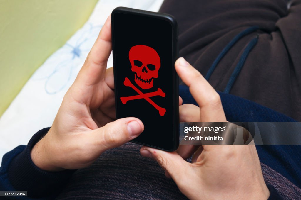 Mann hält ein Telefon in der Hand gehackt. Der rote Schädel brennt auf dem modernen Bildschirm und weist auf eine ernste Gefahr hin. Flacher Stil. Ein Mann hält ein Telefon gehackt