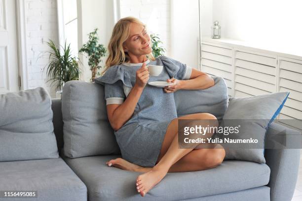 beautiful woman hold cup of coffee relaxing on the couch, sofa in a living room, happy smile day dreaming with tea mug in hands looking out the window. - women arms crossed stock pictures, royalty-free photos & images