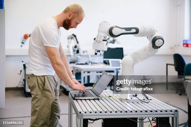 industrie 4.0: junger ingenieur arbeitet an einem roboterarm - rechnerunterstützte fertigung stock-fotos und bilder