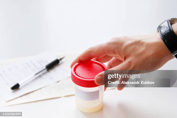 a man puts a medical container with semen analysis labeled, next to the completed form, on a white background. donor sperm for artificial insemination, infertility treatment, planning of children. - sperm stock pictures, royalty-free photos & images
