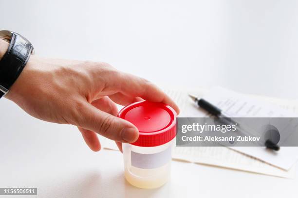 a man puts a medical container with semen analysis labeled, next to the completed form, on a white background. donor sperm for artificial insemination, infertility treatment, planning of children. - sperm stock pictures, royalty-free photos & images