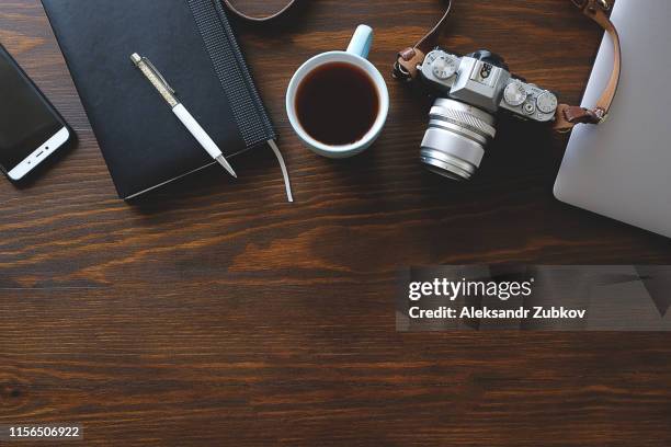 a laptop, a cup of tea, a camera and a notebook lie on a dark wooden table. the workplace of a photographer or a freelancer. copy paste for text. - desk top view stock pictures, royalty-free photos & images
