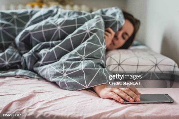 a young woman wakes up the bed. the alarm on the smartphone is ringing - alarme imagens e fotografias de stock