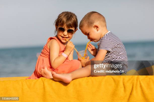 gosses heureux buvant le jus ensemble sur la plage - famille-avec-deux-enfants photos et images de collection