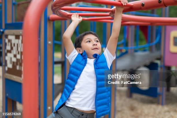 young boy hanging from a play structure at the playground - jungle gym stock pictures, royalty-free photos & images