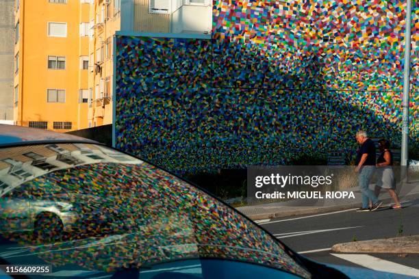 People walk past a mural by French street artist Popay adorning the side of a building in Vigo, northwestern Spain, on July 15, 2019. - Since 2015,...