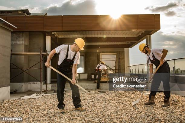 bauarbeiter schaufeln kies, während sie an einem penthouse-balkon arbeiten. - spaten stock-fotos und bilder