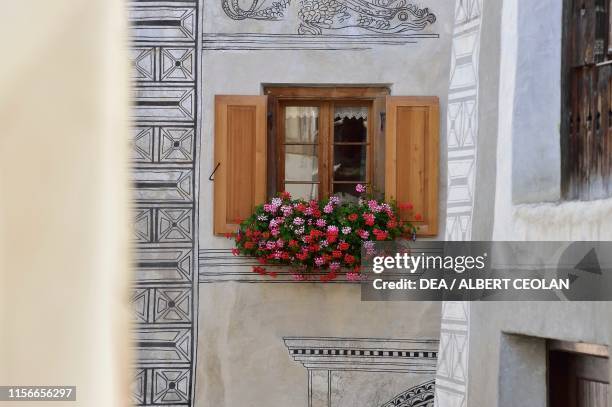 Flowering geraniums and mural paintings on the windows of a house, Ardez, Scuol, Engadin, Canton of Graubunden, Switzerland.