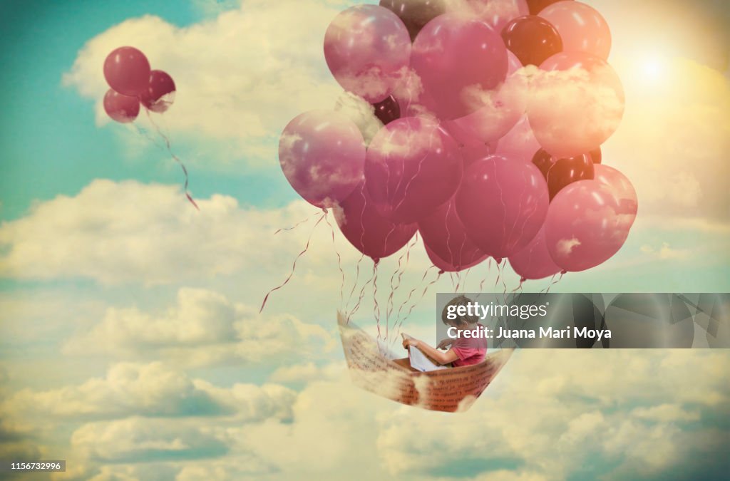 Digital composition, of a boy flying on a paper boat fastened by pink balloons