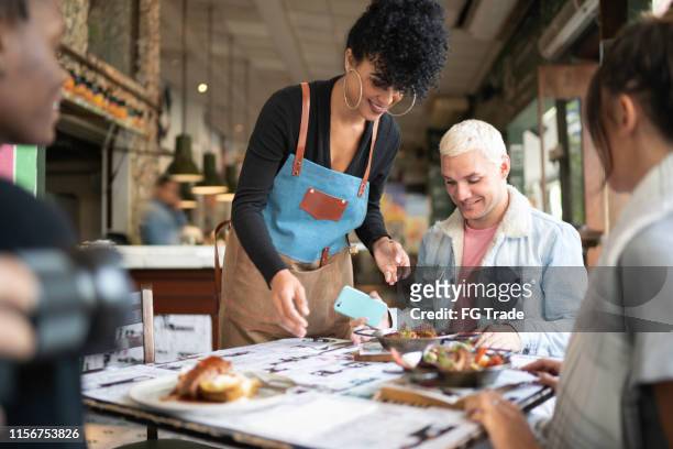 female waiter serving food to a group of friends - black chef stock pictures, royalty-free photos & images
