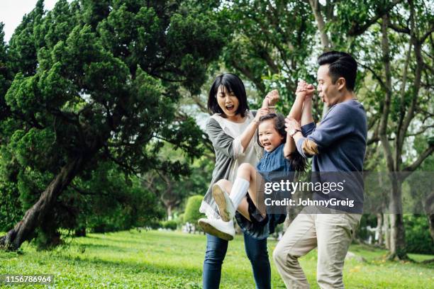 cheerful parents swinging daughter in park - couple swinging stock pictures, royalty-free photos & images