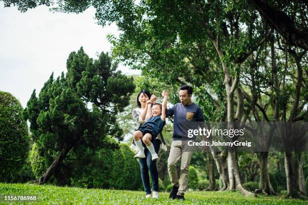 action shot of parents swinging daughter in park - couple swinging stock pictures, royalty-free photos & images