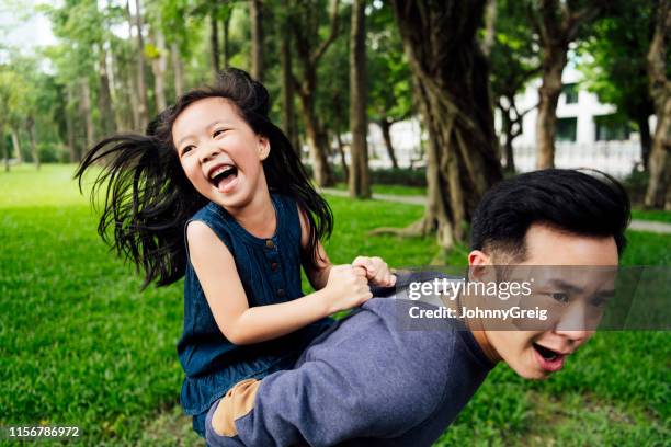 father and daughter having fun piggyback in park - chinese family with one child stock pictures, royalty-free photos & images