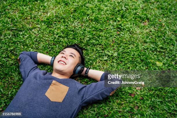 joven acostado sobre hierba usando auriculares - headphones asian fotografías e imágenes de stock