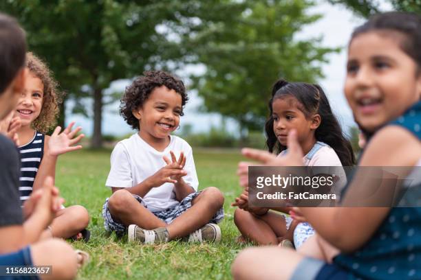 een multi-etnische groep jonge kinderen klappen buiten - sing outside stockfoto's en -beelden