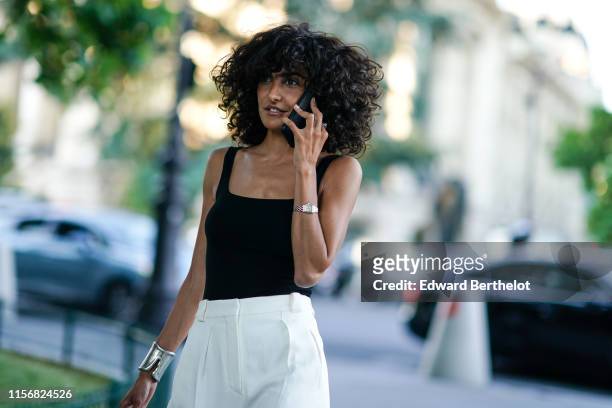 Guest wears a black strappy top, white pants, a silver bangle, outside AMI, during Paris Fashion Week - Menswear Spring/Summer 2020, on June 18, 2019...