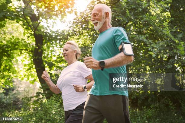 jogging de couples aînés de sourire dans le stationnement - podomètre photos et images de collection
