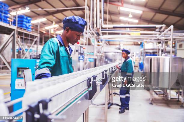 quality inspectors checking milk bottles on the conveyor belt at a dairy plant in africa - minimum wage stock pictures, royalty-free photos & images