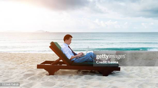 hombre de negocios asiático que usa una computadora portátil en la playa - man on the beach relaxing in deckchair fotografías e imágenes de stock