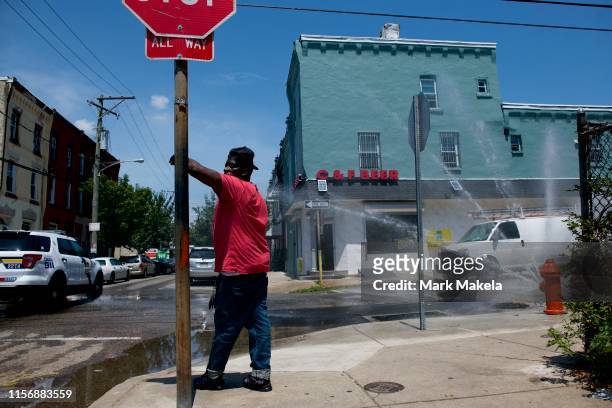 July 20: A police car passes, as a man leans on a stop sign beside a spraying fire hydrant on July 20, 2019 in Philadelphia, PA. With heat indexes...