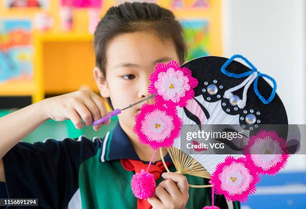 Primary school student makes colorful fan featuring opera mask to welcome the summer solstice on June 19, 2019 in Hohhot, Inner Mongolia Autonomous...