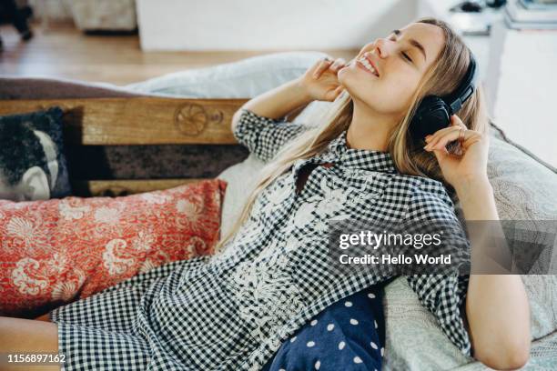 beautiful young woman loving listening to music on the couch - headphones stock pictures, royalty-free photos & images