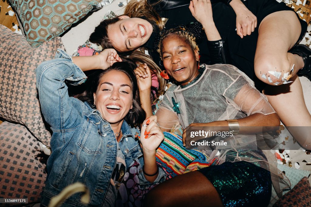 Happy smiling girlfriends relaxing on floor with cushions and confetti