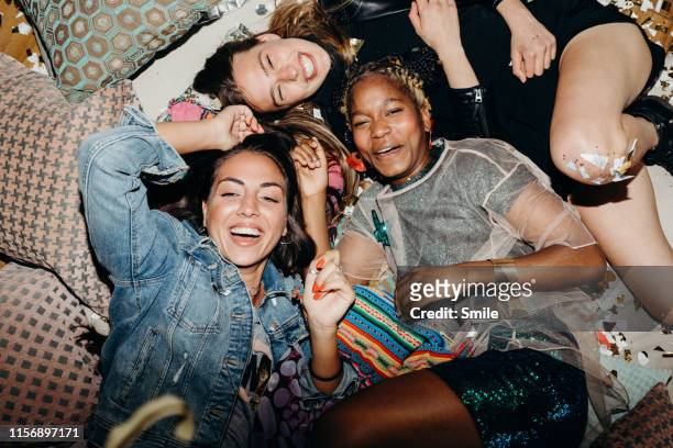 happy smiling girlfriends relaxing on floor with cushions and confetti - party stock pictures, royalty-free photos & images